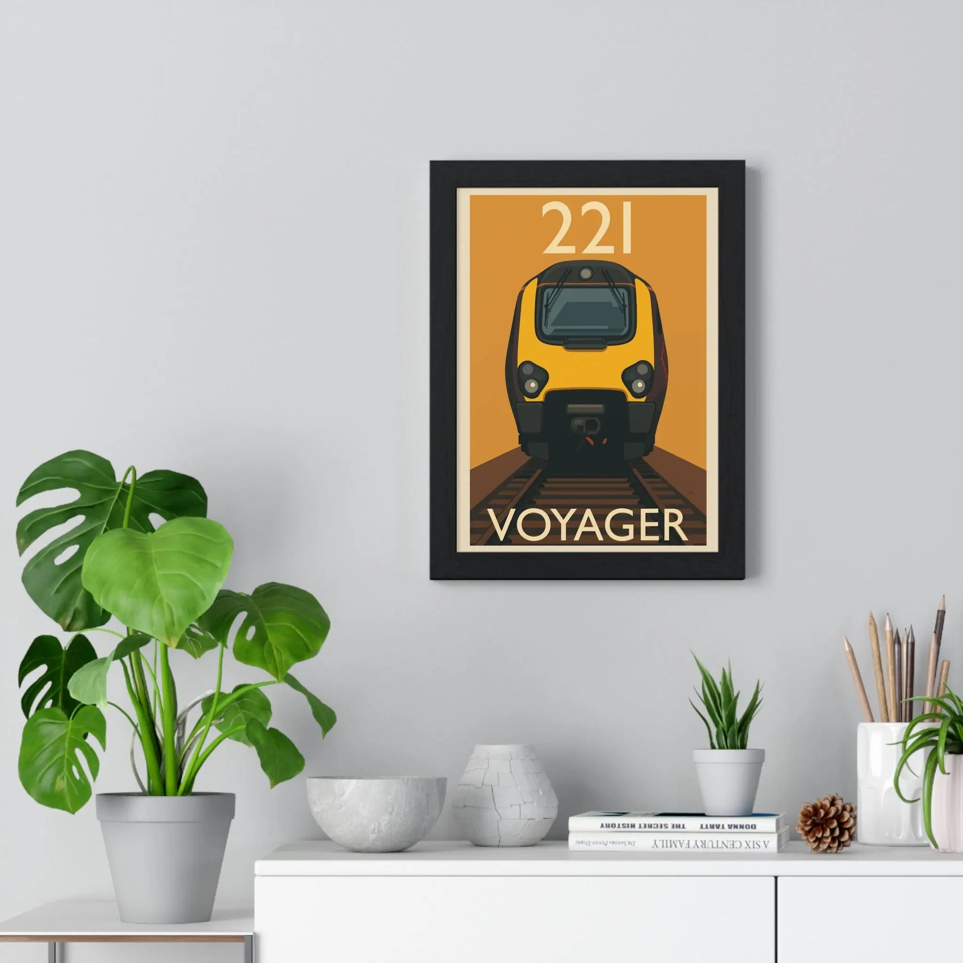 Framed poster of a train labeled '221 Voyager' on a wall with decorative items below.