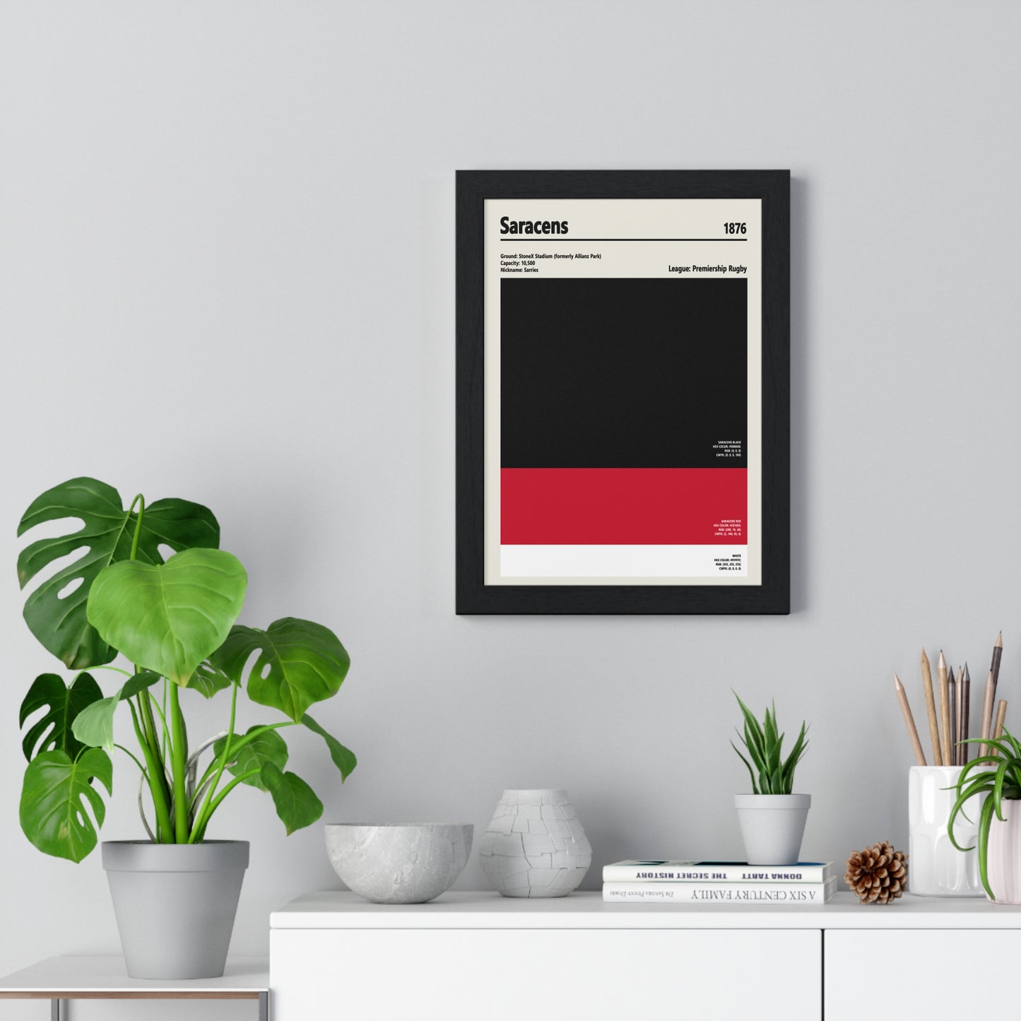 Framed poster of Saracens rugby team on a wall with plants and decor below.