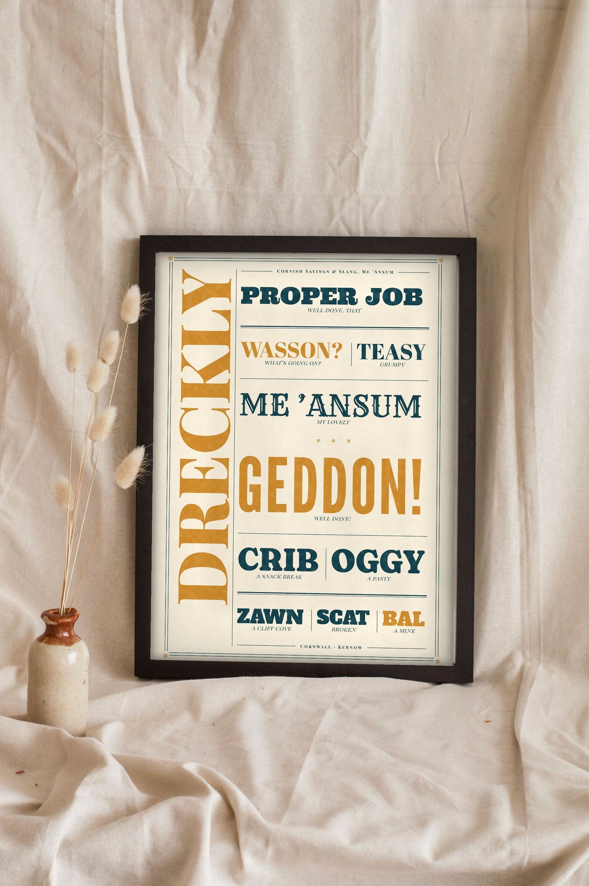 Cornish Slang Print in a black frame propped up on linen
