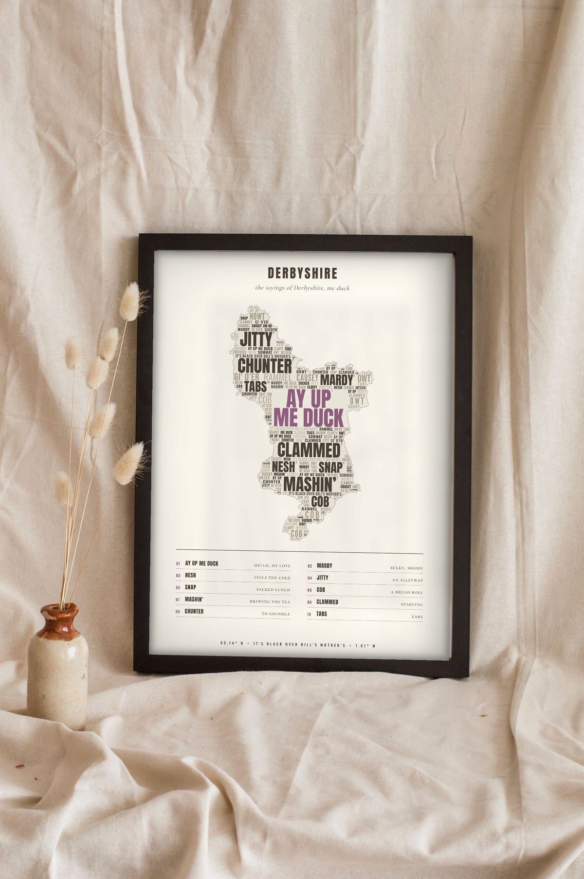 Derbyshire Sayings Poster in a black frame propped up on linen