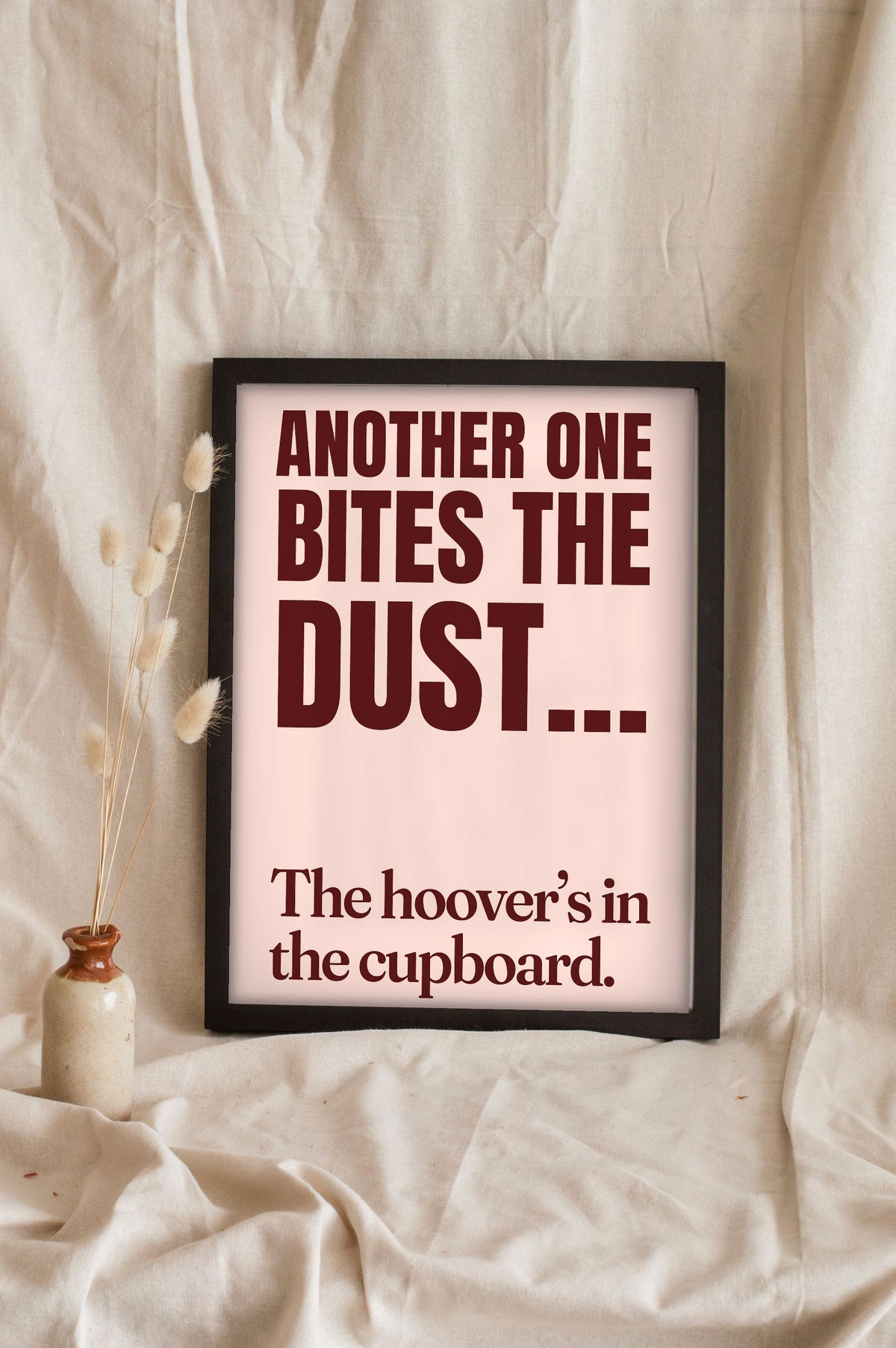Funny Another One Bites the Dust lyric print in a black frame propped up on linen