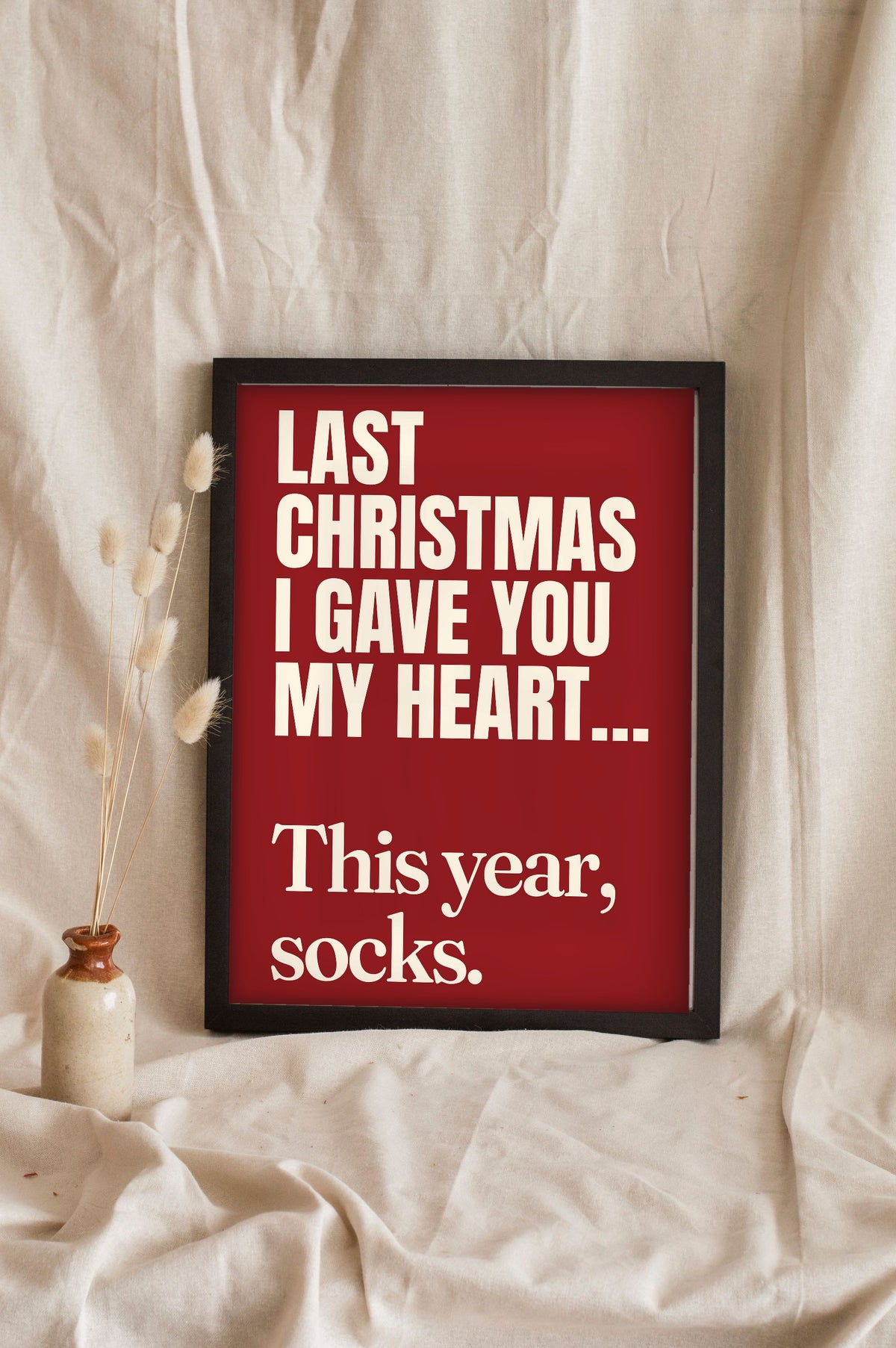 Funny Last Christmas lyric print in a black frame propped up on linen