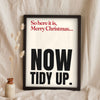 Funny Merry Xmas Everybody lyric print in a black frame propped up on linen