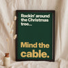 Funny Rockin' Around the Christmas Tree lyric print in a black frame propped up on linen