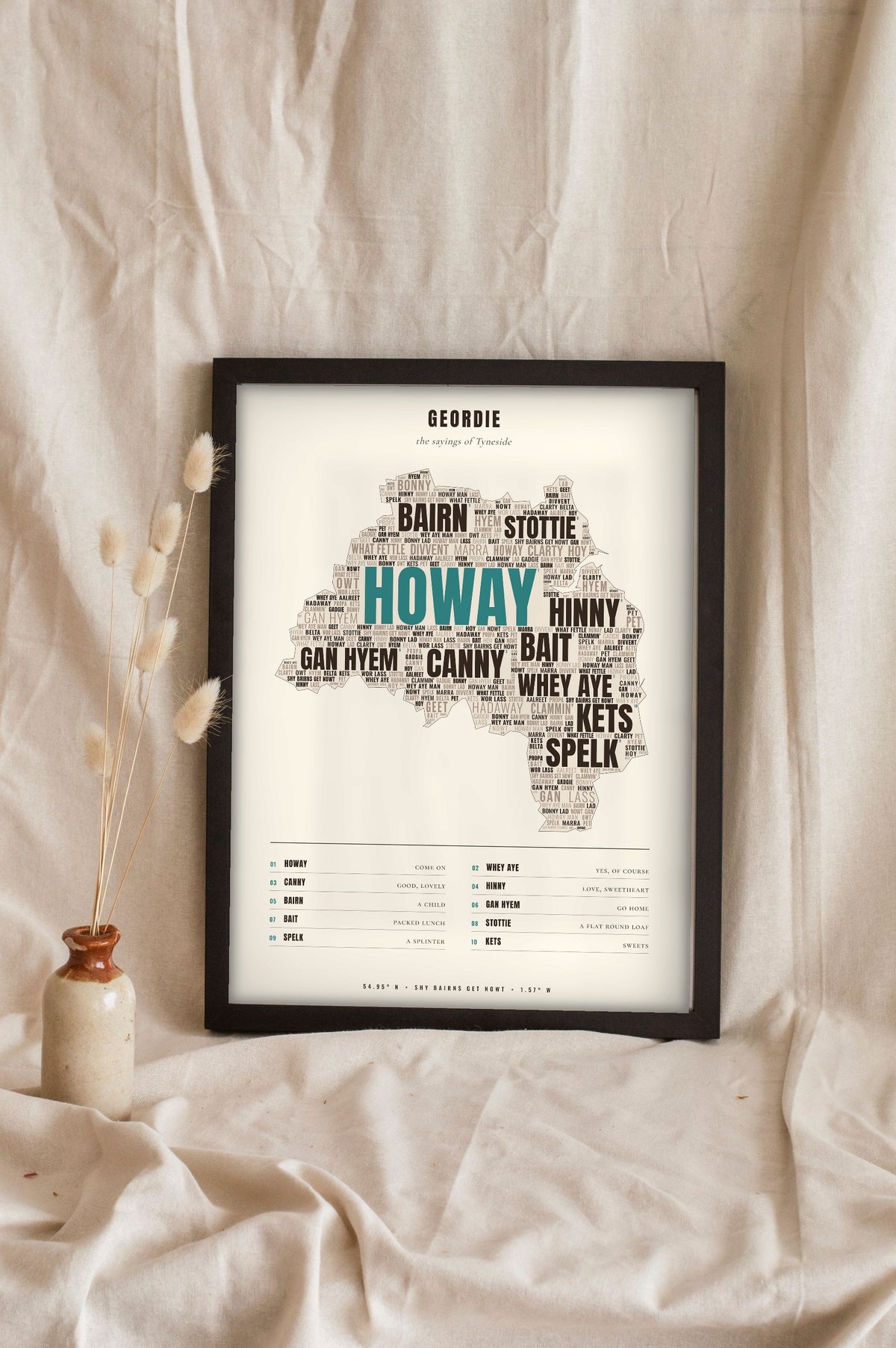 Geordie Sayings Print in a black frame propped up on linen