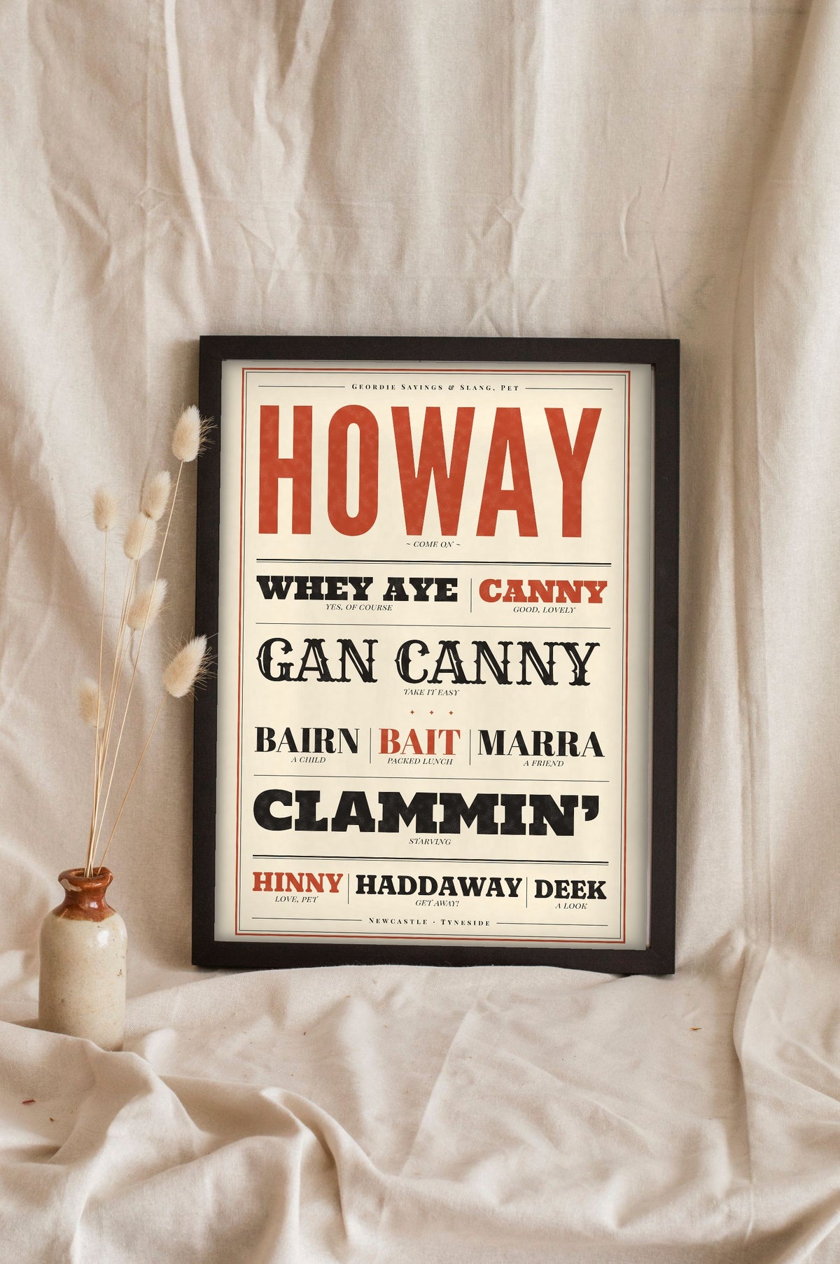 Geordie Slang Print in a black frame propped up on linen