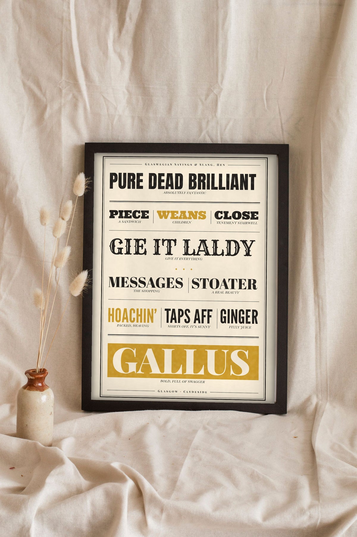 Glasgow Sayings Print in a black frame propped up on linen