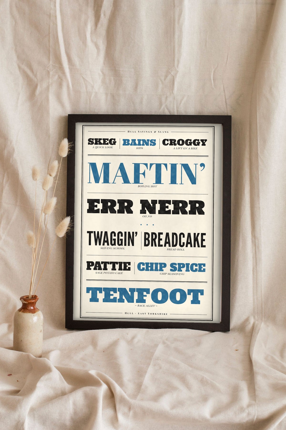 Hull Sayings Print in a black frame propped up on linen