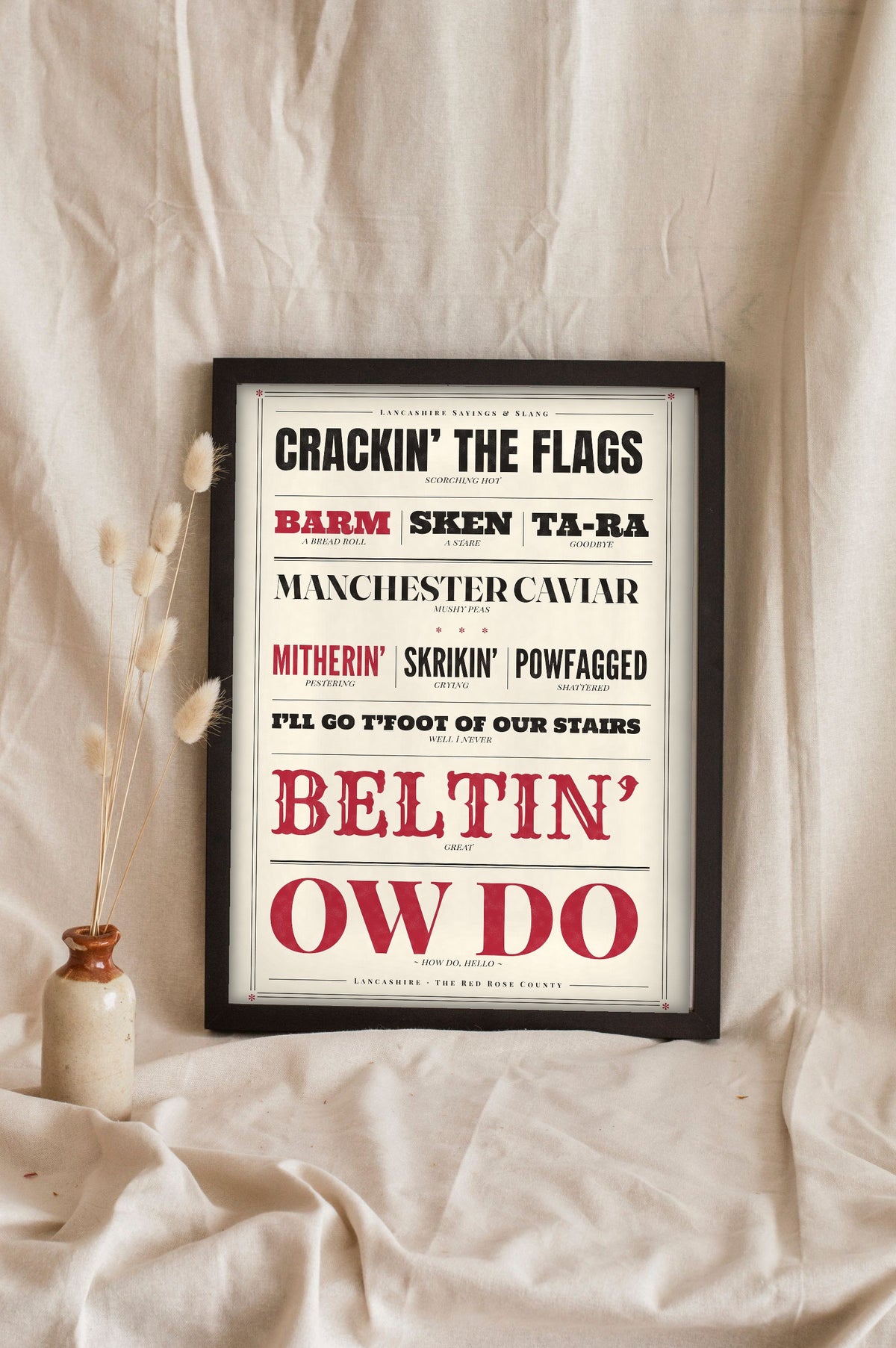 Lancashire Slang Print in a black frame propped up on linen