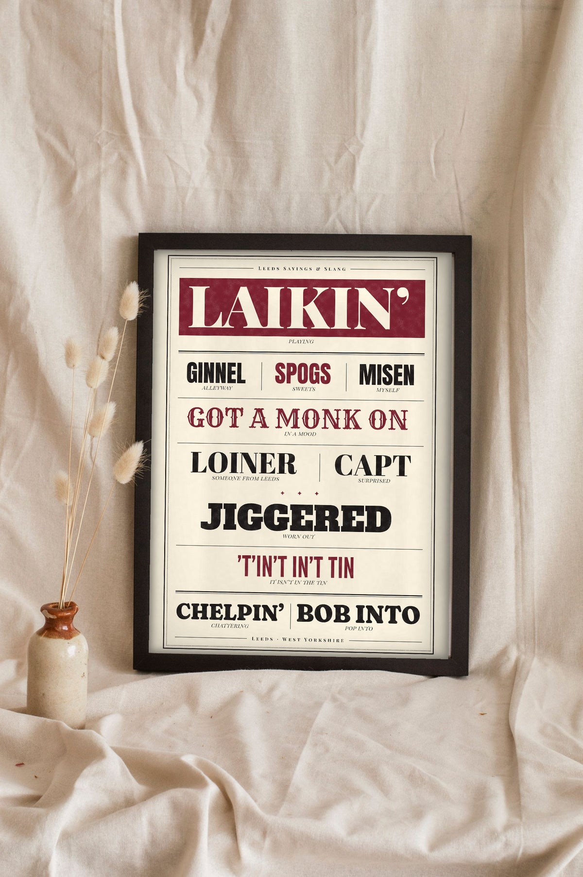 Leeds Sayings Print in a black frame propped up on linen