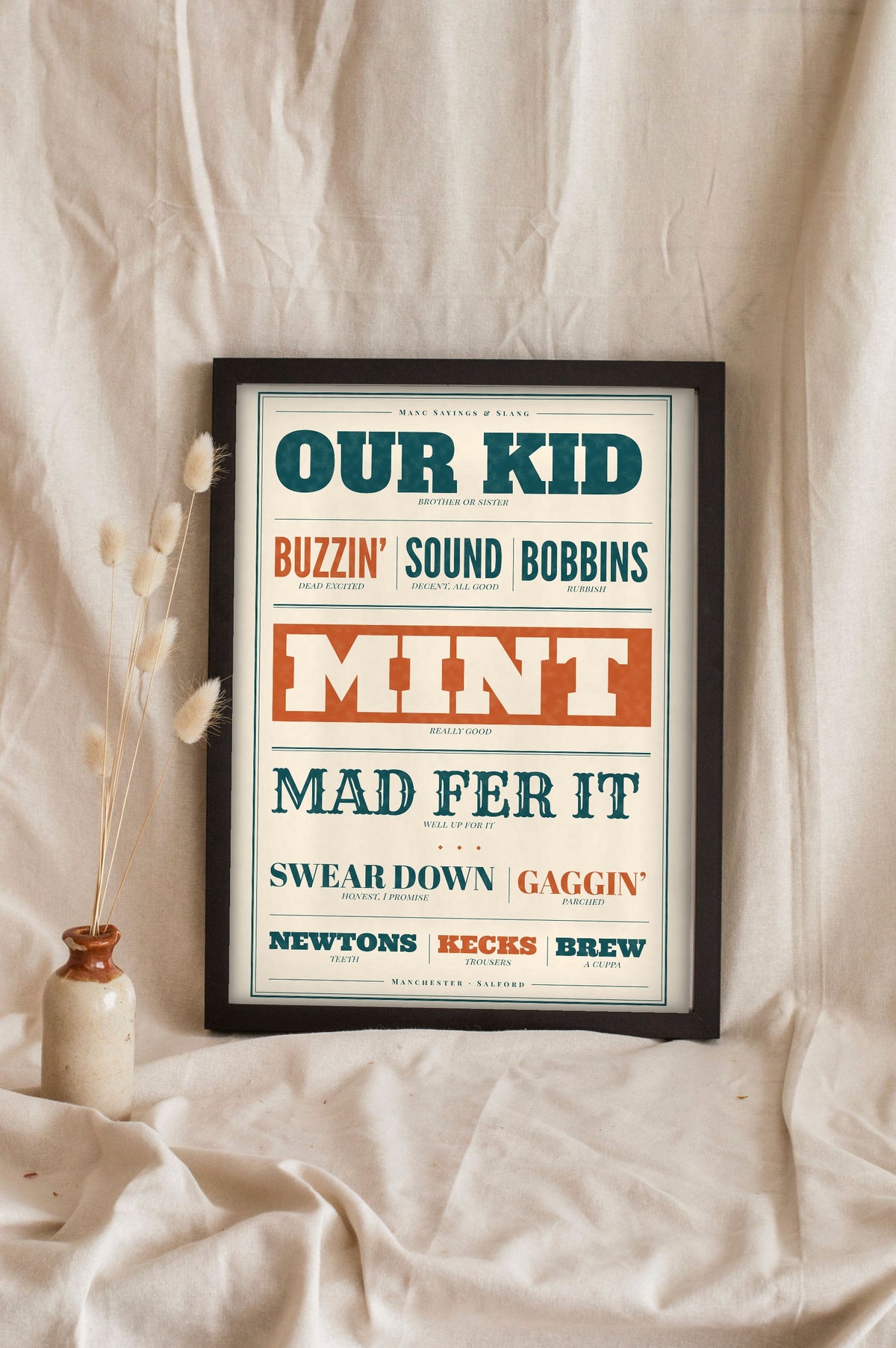 Manchester Slang Print in a black frame propped up on linen