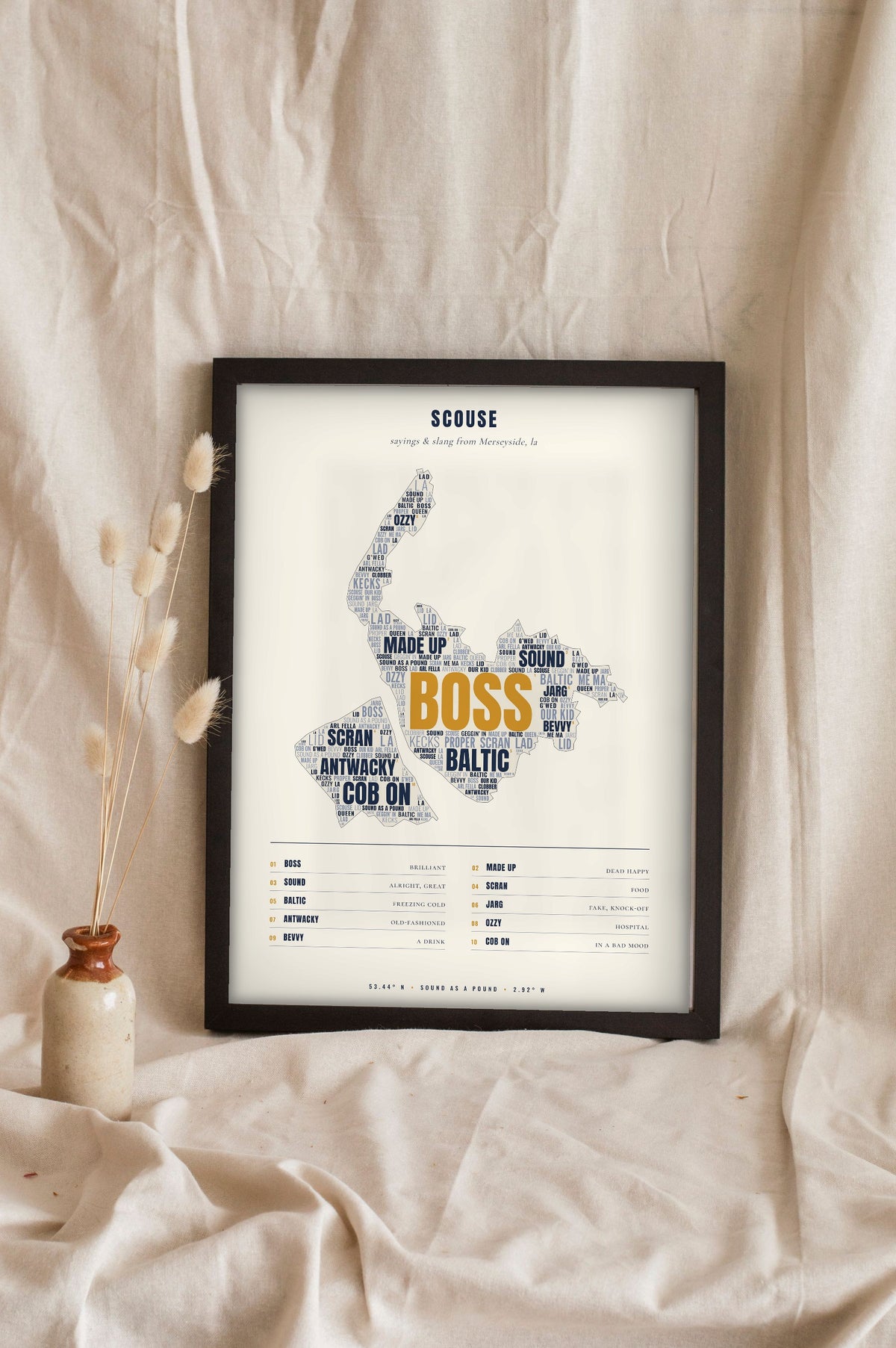 Merseyside Sayings Print in a black frame propped up on linen