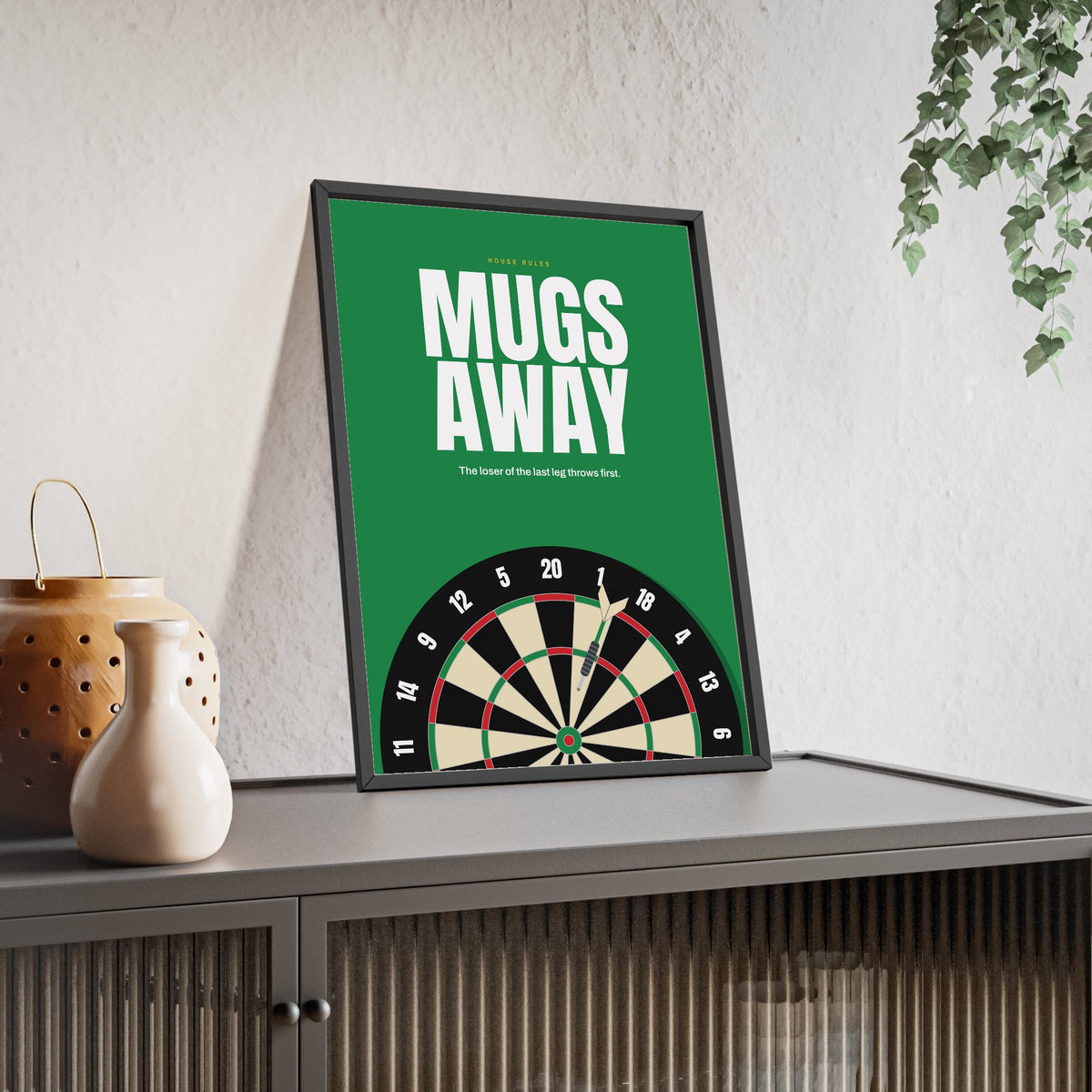 Mugs Away Darts print framed and leaning on a sideboard