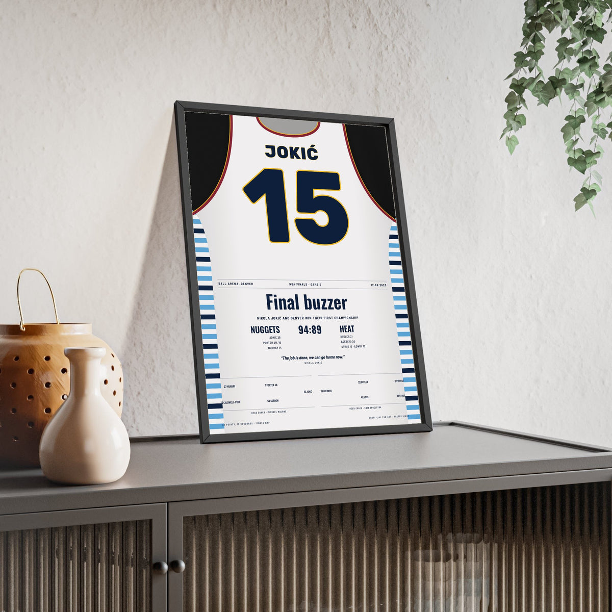 Nikola Jokić 2023 NBA Finals Poster - Denver Nuggets 15 First Championship Jersey Print framed and leaning on a sideboard