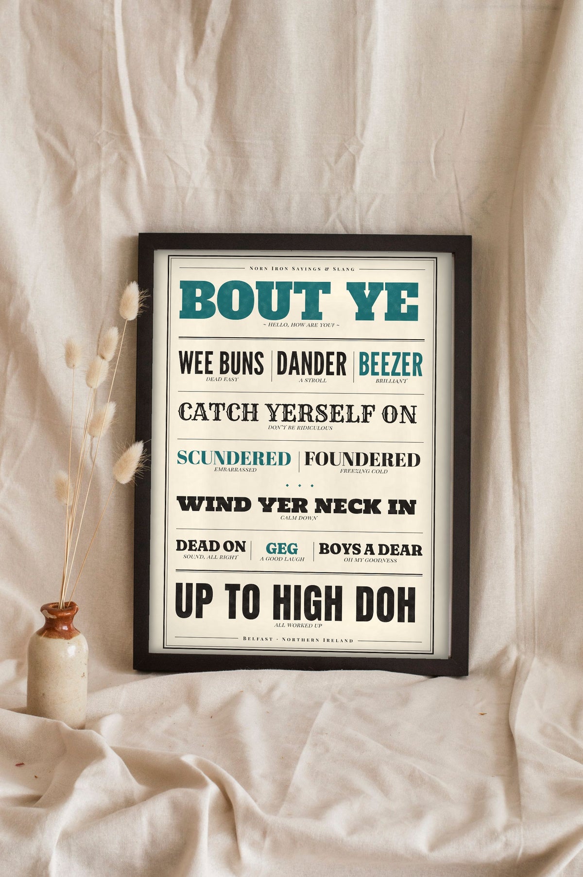 Northern Irish Slang Print in a black frame propped up on linen