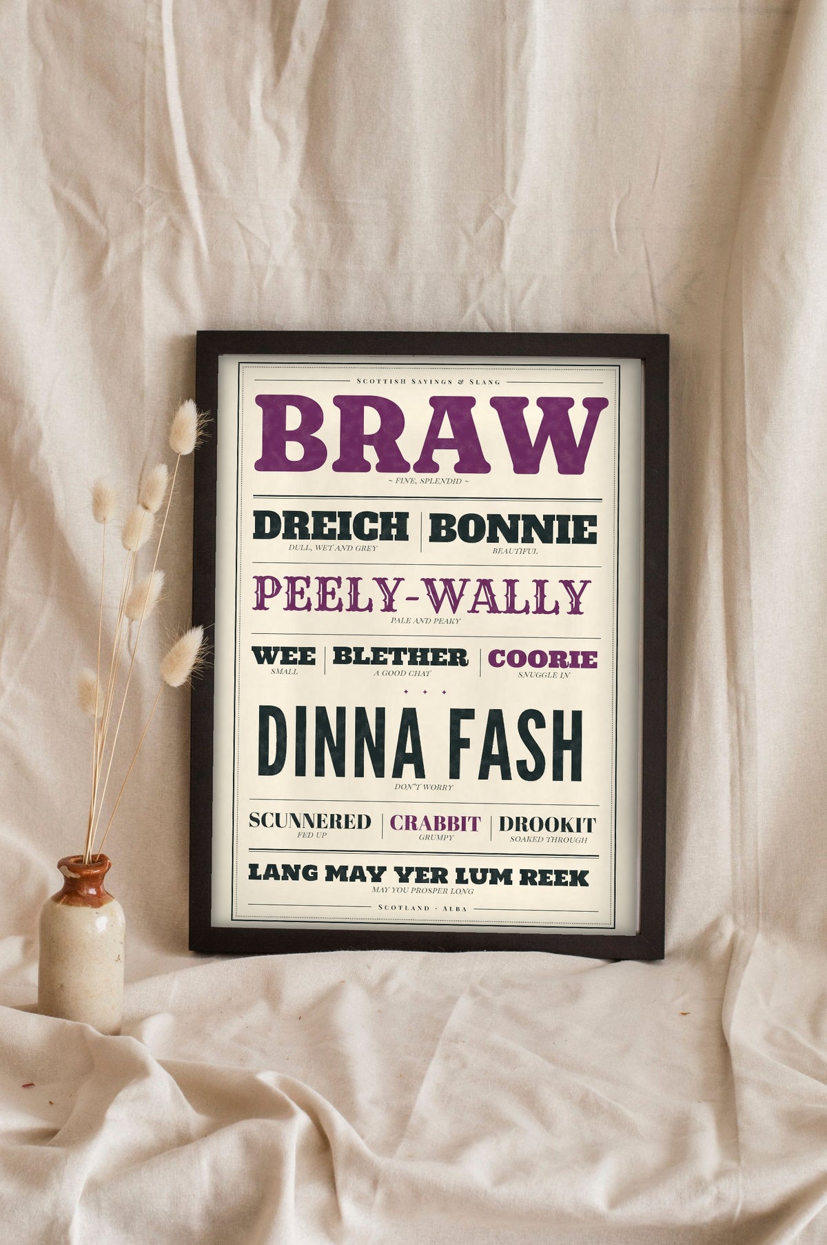 Scottish Slang Print in a black frame propped up on linen