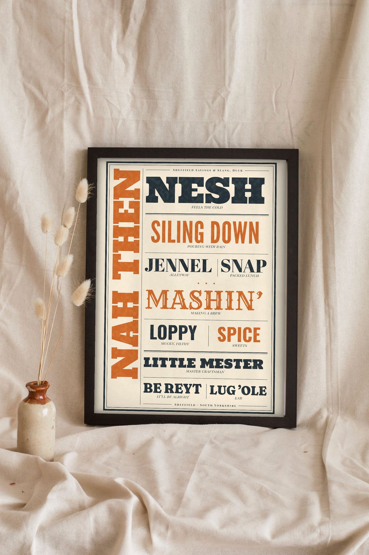 Sheffield Sayings Print in a black frame propped up on linen