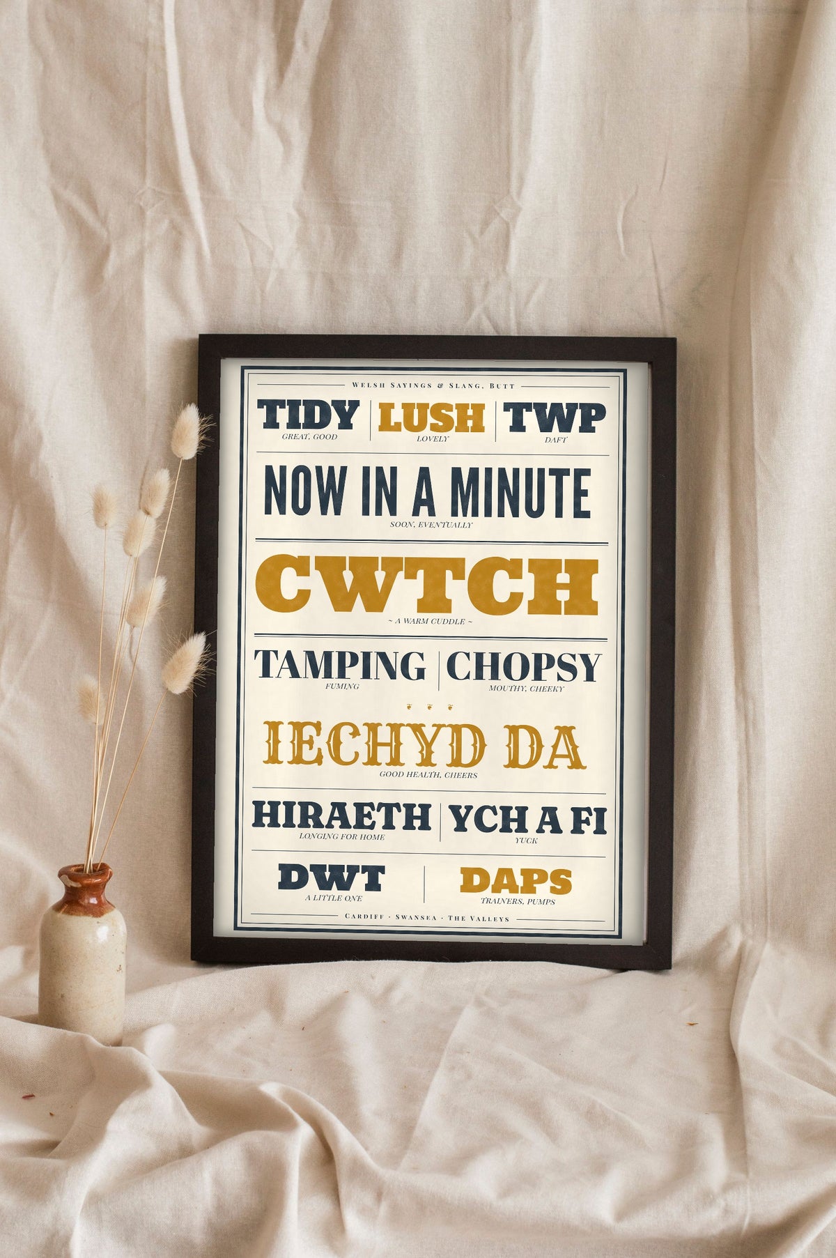 Welsh Slang Print in a black frame propped up on linen