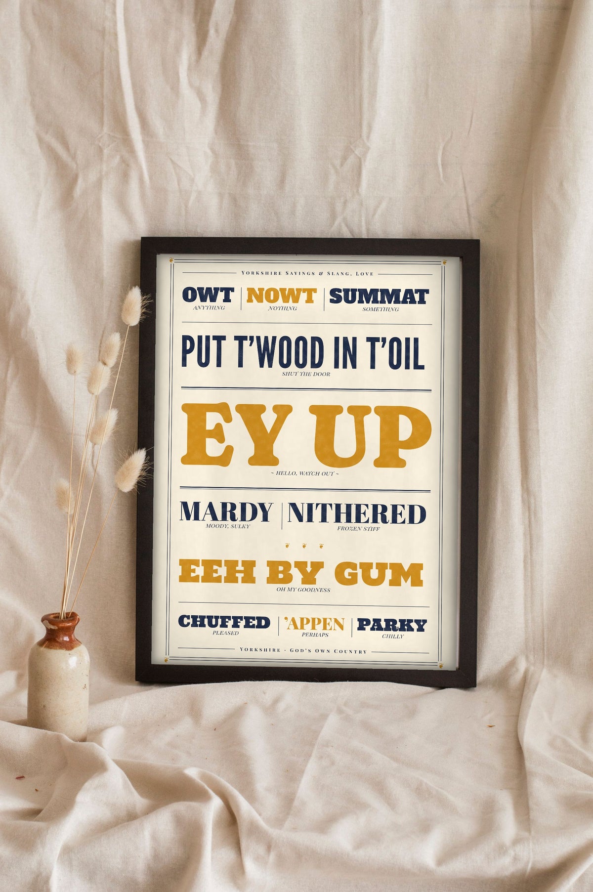 Yorkshire Slang Print in a black frame propped up on linen